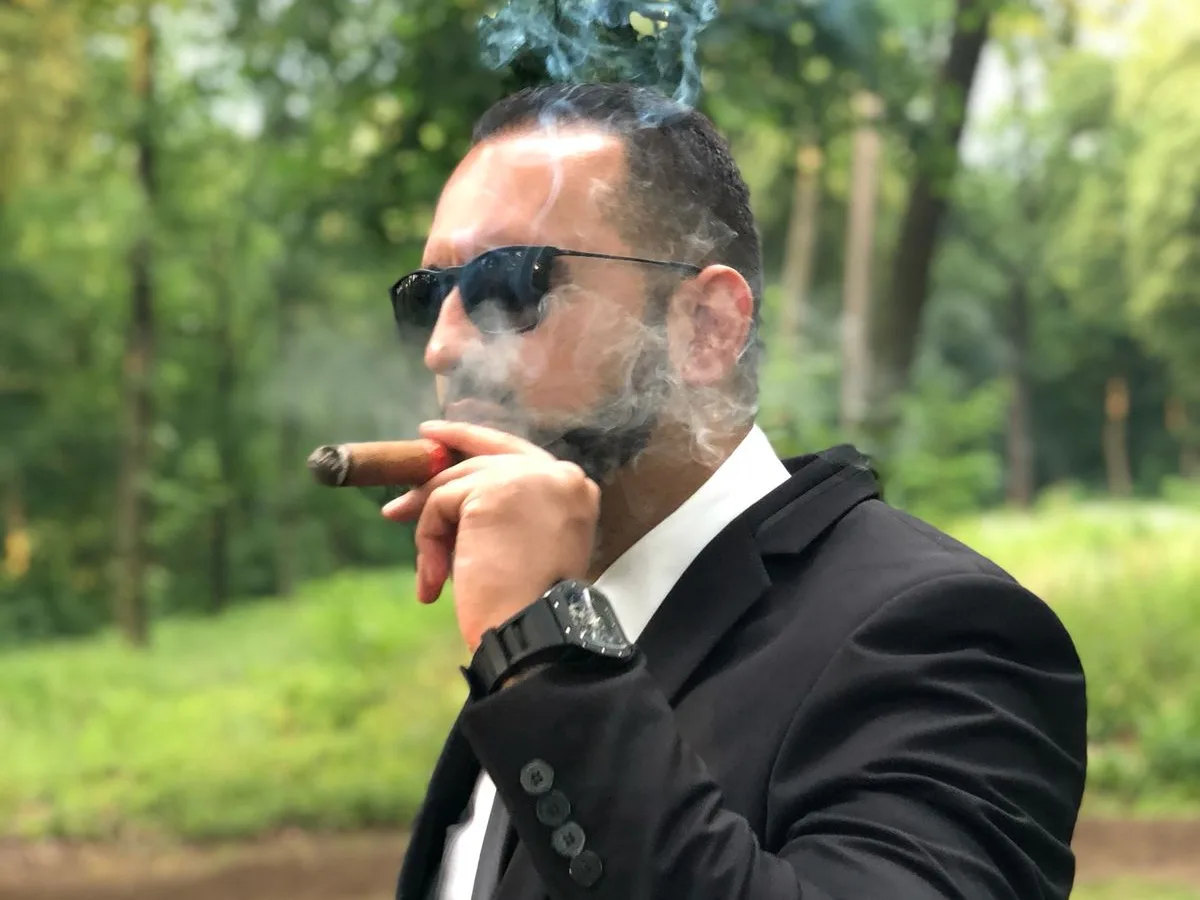 Arash Rezaei outdoors in a black suit and sunglasses, composed and unhurried.