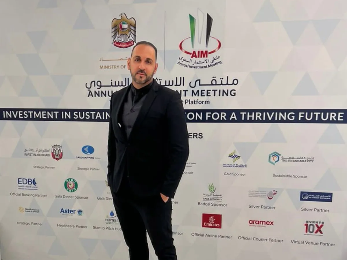 Arash Rezaei standing in a black suit at an Annual Investment Meeting backdrop.