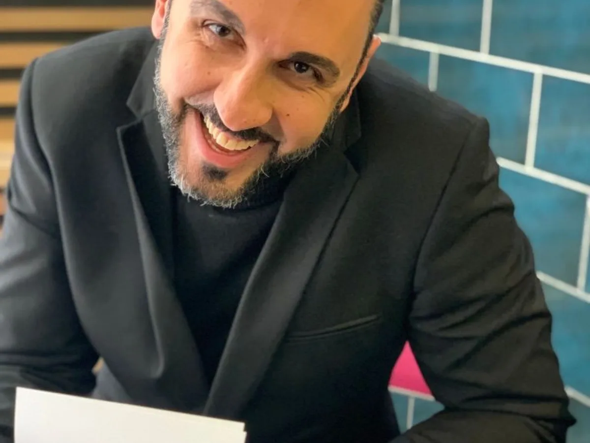 Arash Rezaei smiling as he signs a copy of his book, Be Epic.